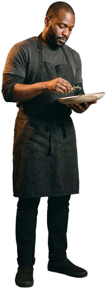 A chef plating the last dish at the pass under copper heat lamps