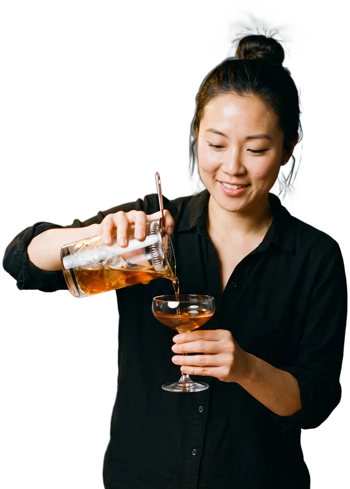 A mixologist pouring a cocktail into a coupe at a marble bar